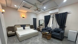 A modern hotel room with a large bed, two armchairs, a small table, and a ceiling fan. - Prime View Guest House (Islamabad)