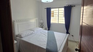 Een slaapkamer met een bed, een nachtkastje, een lamp, een plafondventilator en een raam met gordijnen.