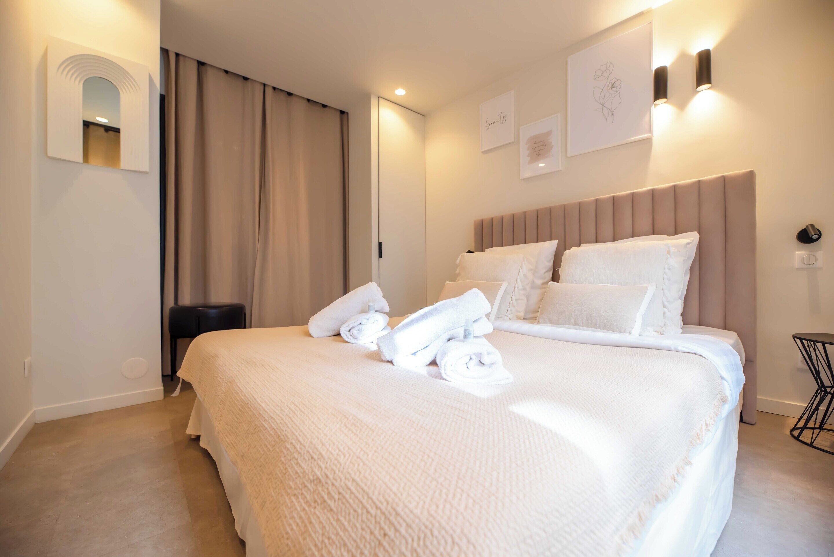 Una cama bien tendida con sábanas y almohadas blancas, una mesita de noche y un aplique de pared.