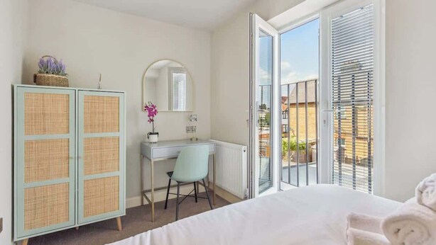 Une chambre à coucher comprenant un lit, un bureau, une chaise, une armoire et une grande fenêtre avec des stores.