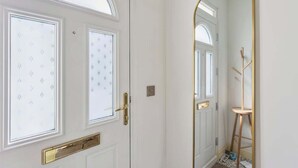 Une porte blanche avec une poignée dorée, un miroir avec un cadre doré et une échelle en bois appuyée contre le mur.