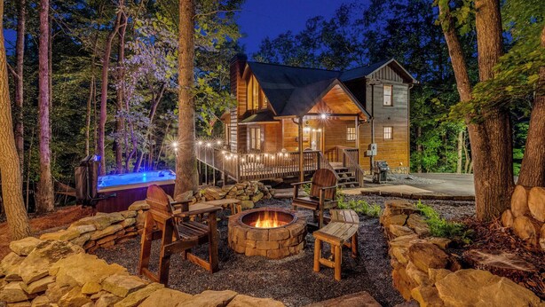 A cabin with a hot tub, outdoor seating, and a fire pit surrounded by rocks.
