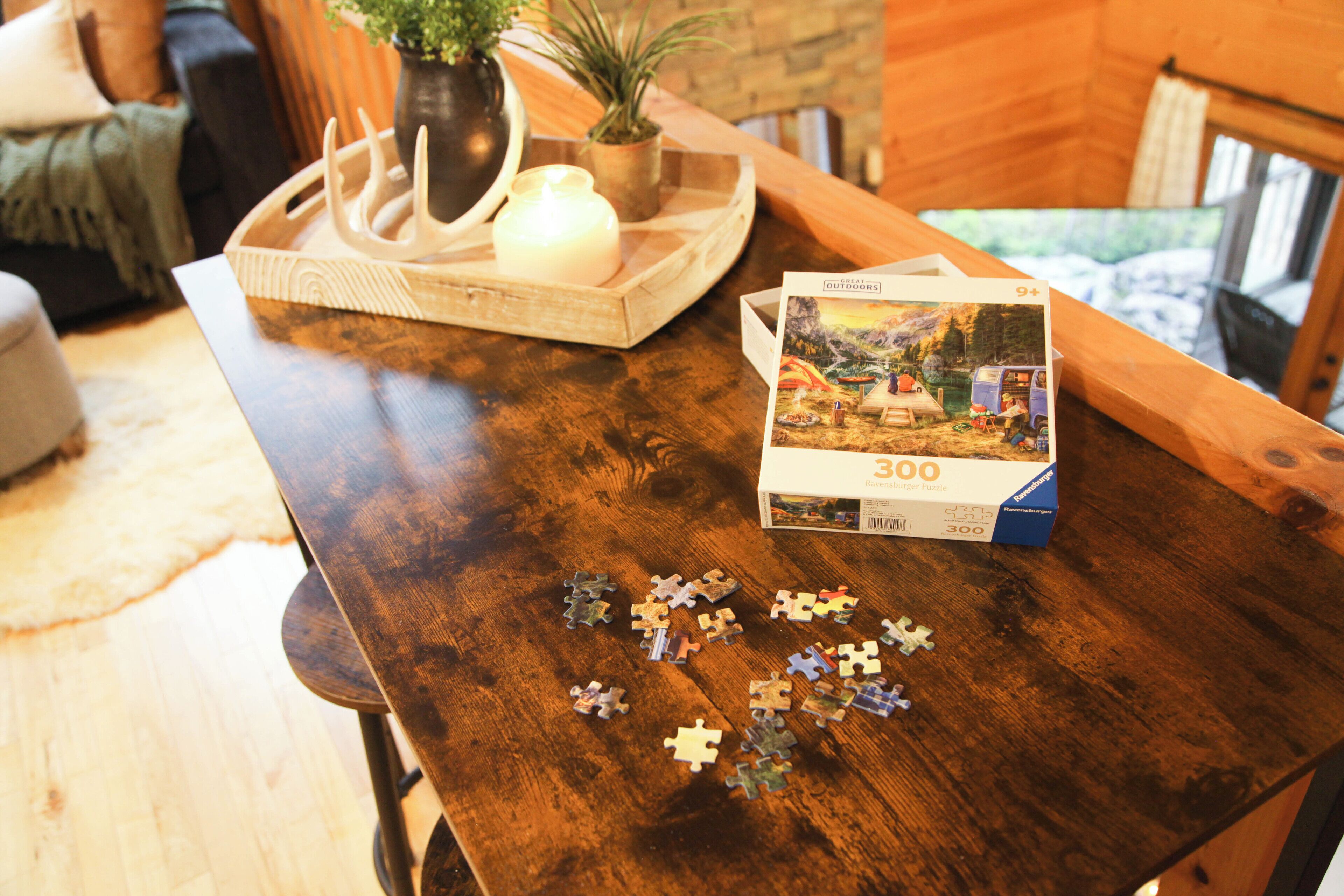 A wooden table with a puzzle box and pieces, a candle, and a tray with decorative items.