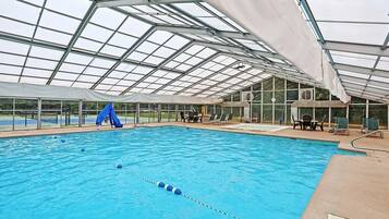 A large indoor swimming pool with a glass ceiling and lounge chairs around the perimeter.