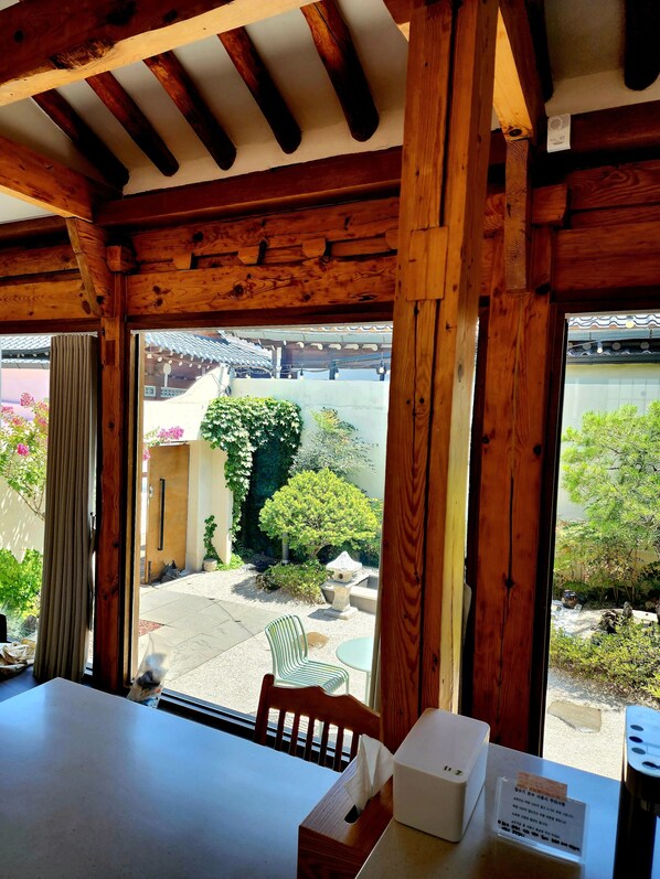 Un intérieur en bois avec une table, des chaises et une vue sur un jardin agrémenté d’un arbre et d’une mangeoire à oiseaux.