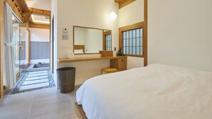A bedroom with a large bed, a wooden headboard, a bedside table, a mirror, and a window with wooden frames.