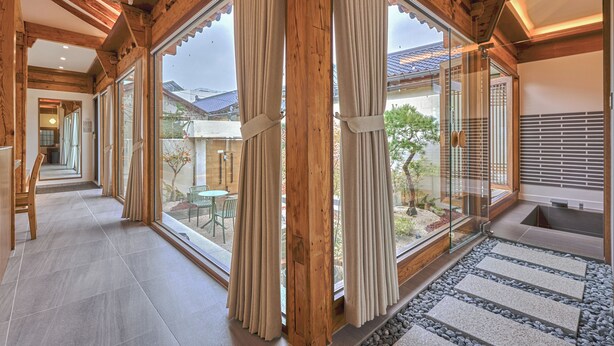 A spacious interior with large sliding glass doors, wooden beams, and a stone pathway leading to an outdoor seating area.