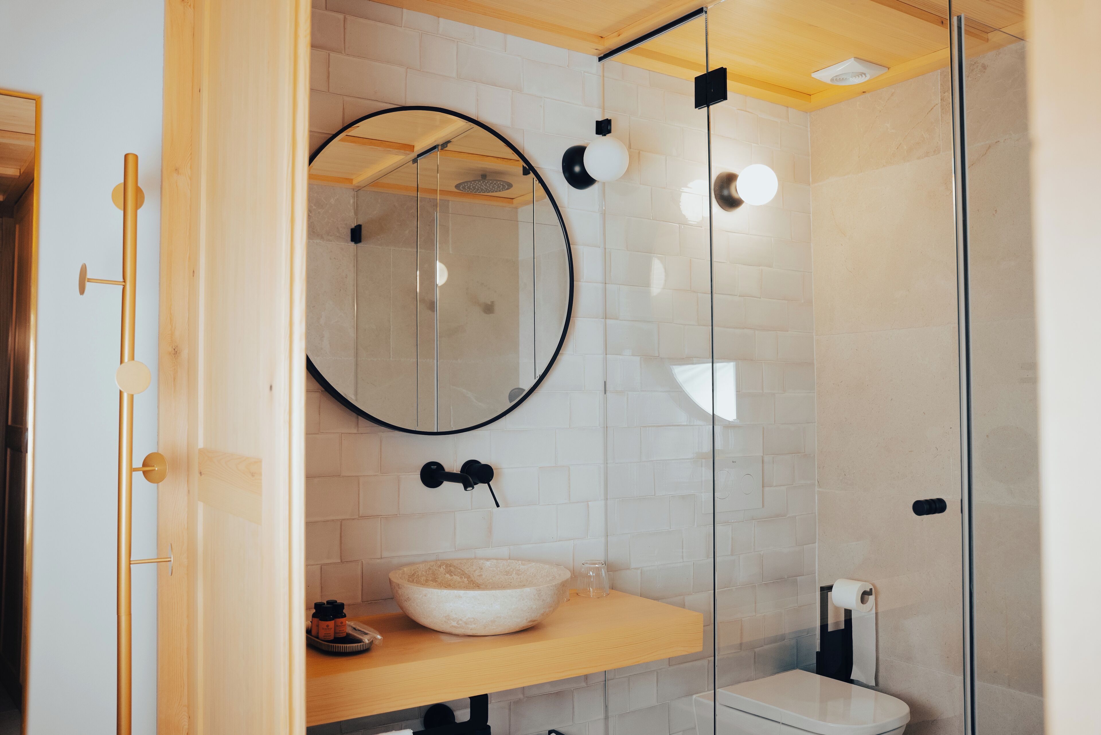 Un baño moderno con ducha de vidrio, un espejo redondo y un mueble de tocador de madera con lavabo.