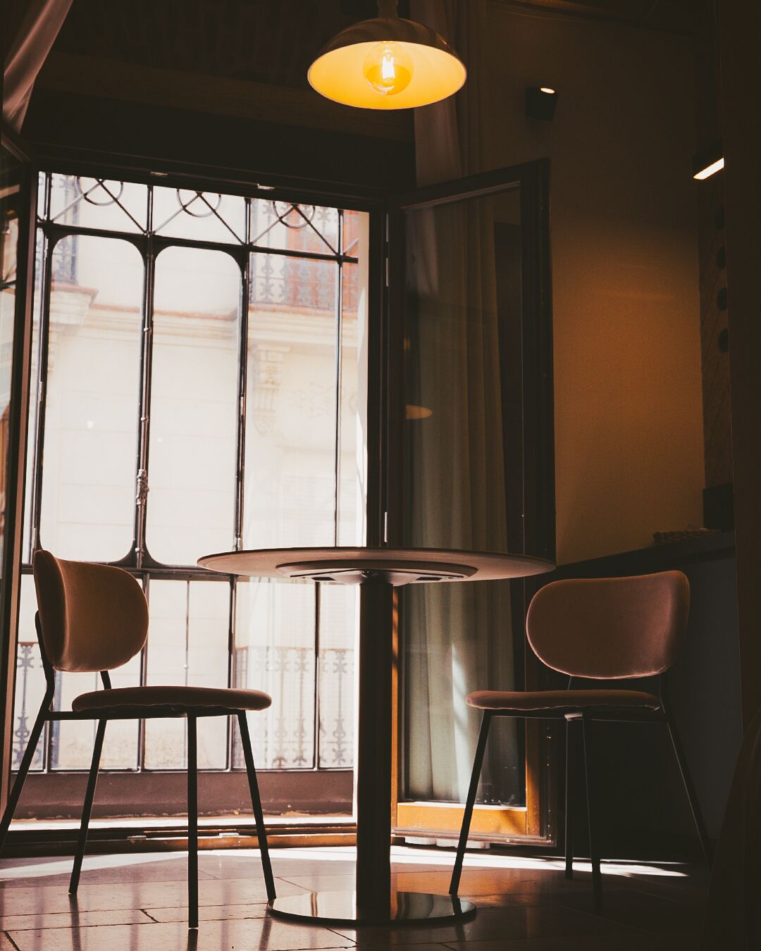 A room with a round table and two chairs, a window with metal bars, and a hanging light fixture.