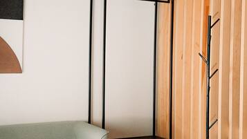 Una habitación de esquina con un sofá blanco, una pequeña mesa redonda, un soporte de metal negro y un separador de madera con listones.