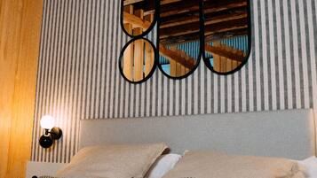 A hotel room with a striped wall, a bed with patterned pillows, and a wooden ceiling beam.