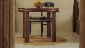 A wooden dining table with a bowl of lemons, a chair, and a hanging light fixture in a hallway.