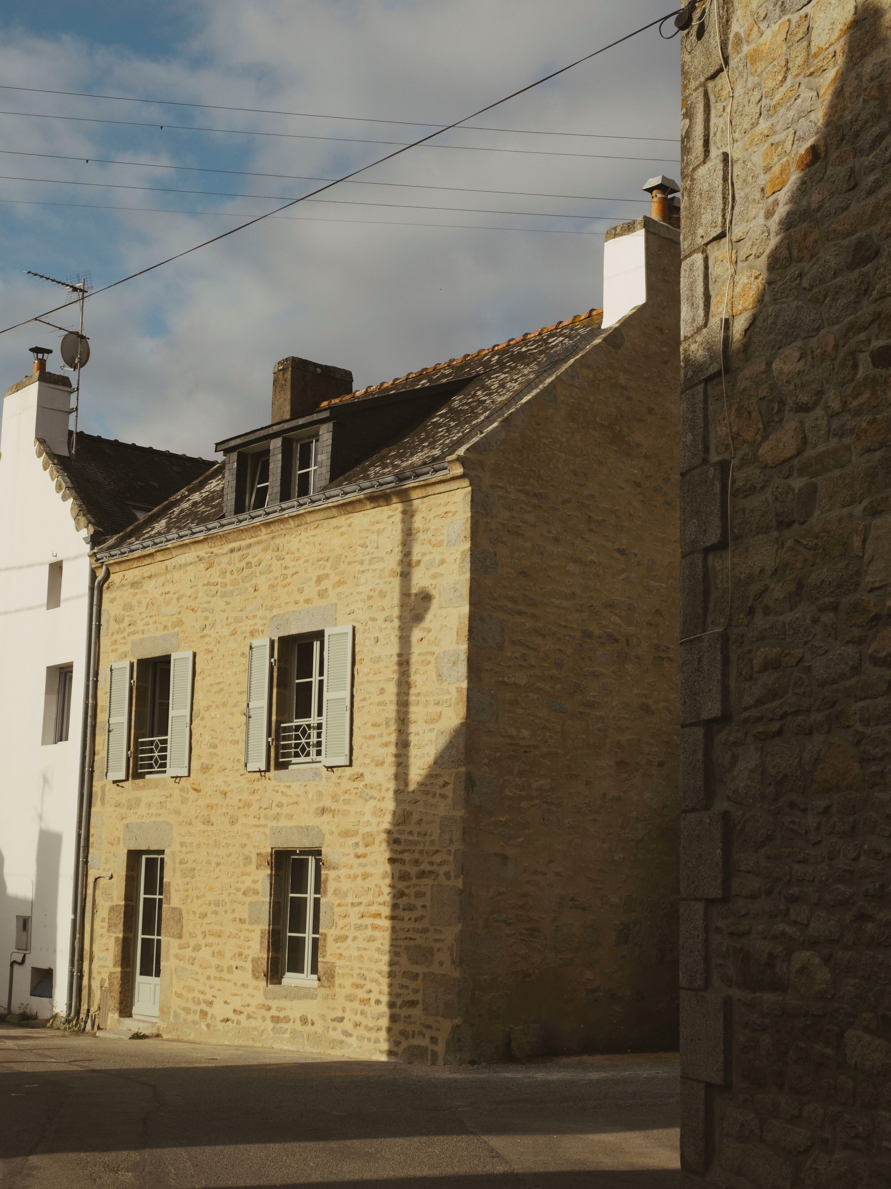 A stone building with a tiled roof, a small window with shutters, and a chimney.