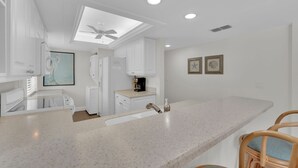 Una cocina moderna con armarios blancos, encimera de granito y ventilador de techo.
