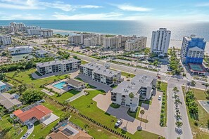 An aerial view of a coastal residential area with multiple high-rise buildings, a central road, and a beach in the background.