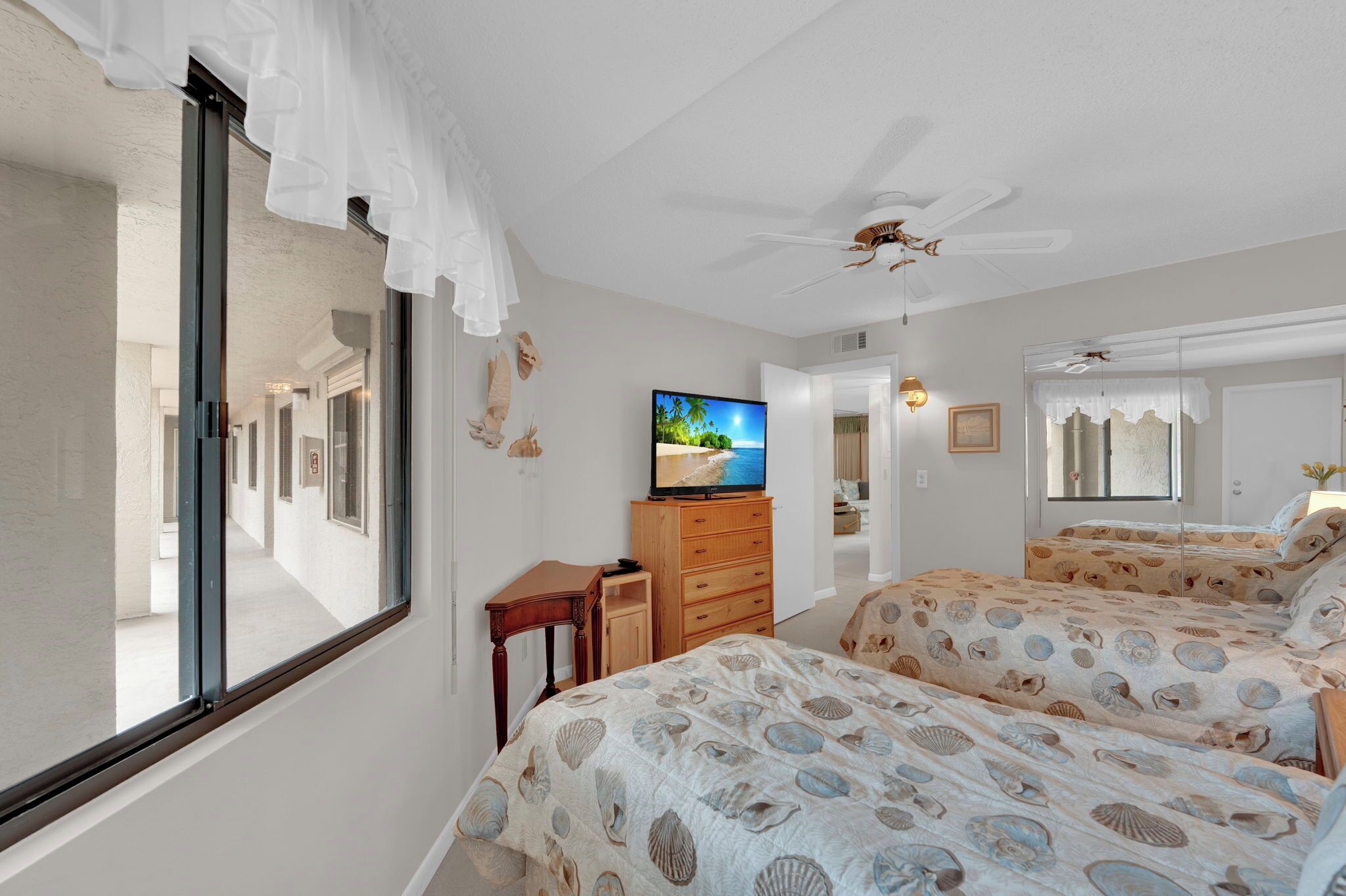 A bedroom with two beds, a television, and a ceiling fan.