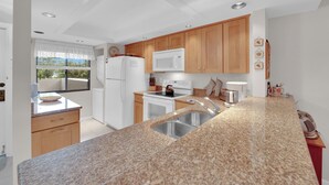A modern kitchen with granite countertops, wooden cabinets, a built-in microwave, and a stainless steel sink. - SUMMER/FALL DISCOUNT!!!  2B/2B Fairview Isles 123 Condo, Walk to Beach, Heated Pool! (Fort Myers Beach)