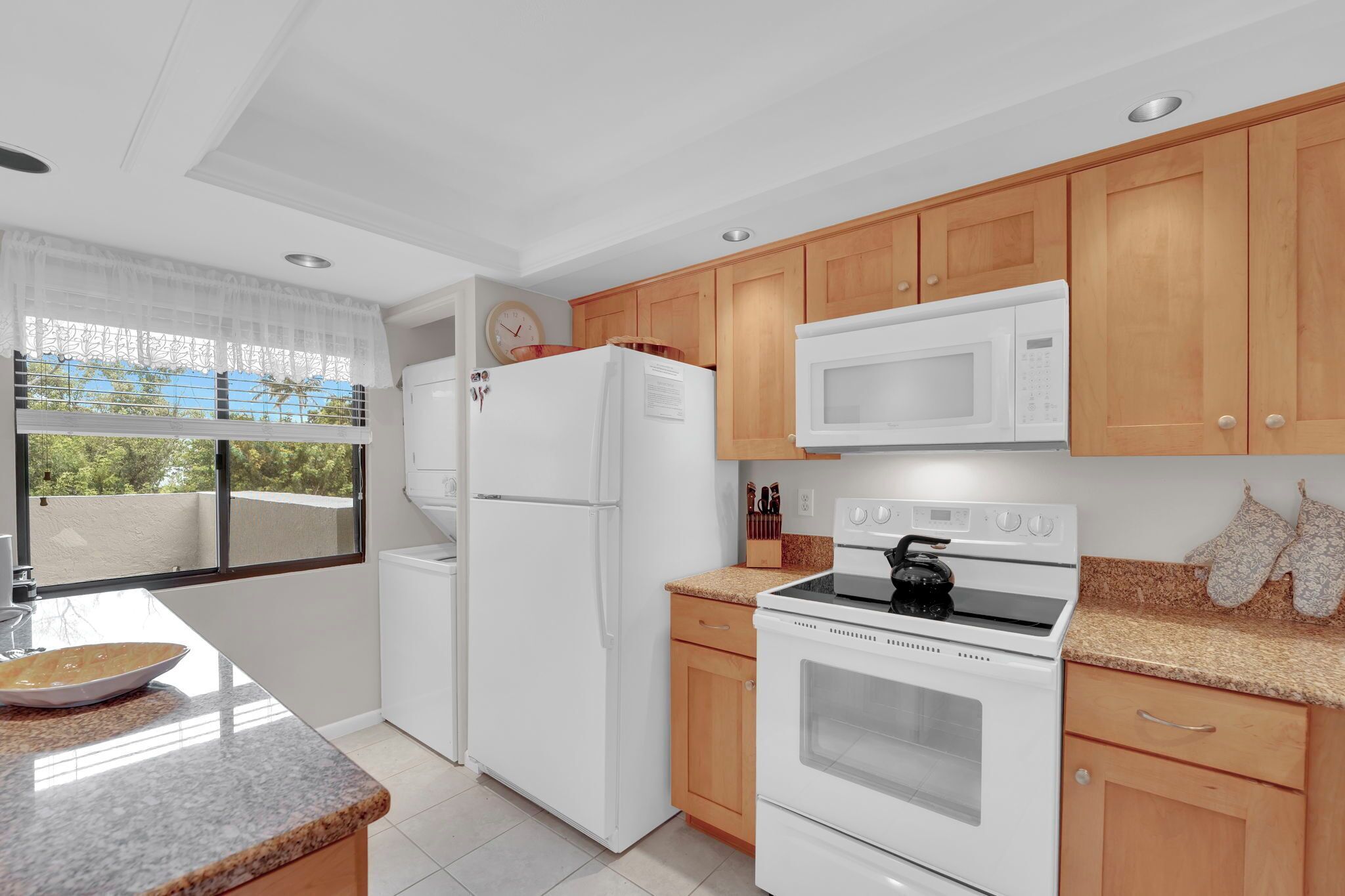 A modern kitchen with white appliances, wooden cabinets, and a large window.