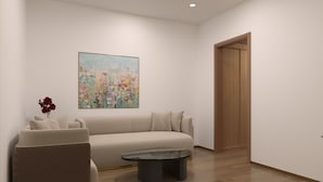 A modern living room with a beige sofa, a small armchair, and a coffee table. A colorful painting is on the wall, and a wooden door is visible. - Playotel Grande Rau (Indore)