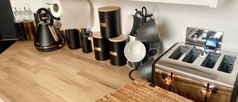 A kitchen with a coffee maker, tea kettle, and various containers.