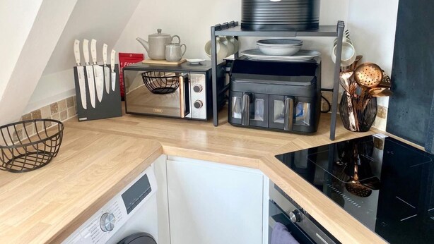A compact kitchen with a microwave, toaster, and kettle on the countertop, a washing machine, and a sink. - Central Tenby 3 Bed Apt Sleeps 6 to 8 Dog Friendly (Tenby)