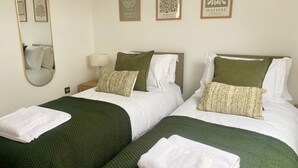 Two twin beds with green blankets and white pillows, a bedside lamp, and framed artwork on the wall. - Central Tenby 3 Bed Apt Sleeps 6 to 8 Dog Friendly (Tenby)
