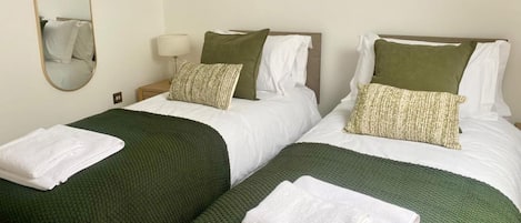Two twin beds with green blankets and white pillows, a bedside lamp, and framed artwork on the wall.