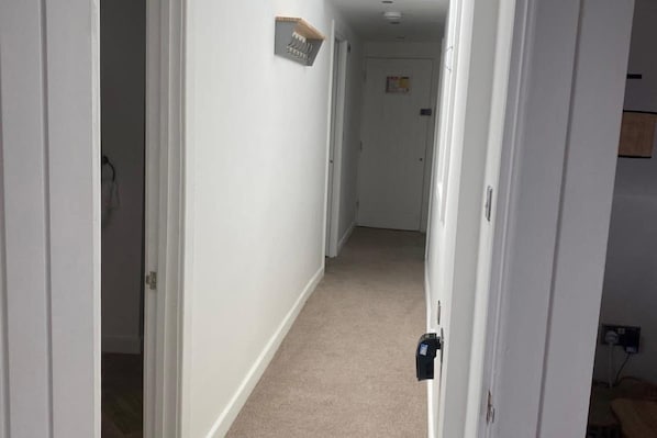 A narrow hallway with white walls and a beige carpet. There is a door at the end of the hallway with a sign above it. - Central Tenby 3 Bed Apt Sleeps 6 to 8 Dog Friendly (Tenby)