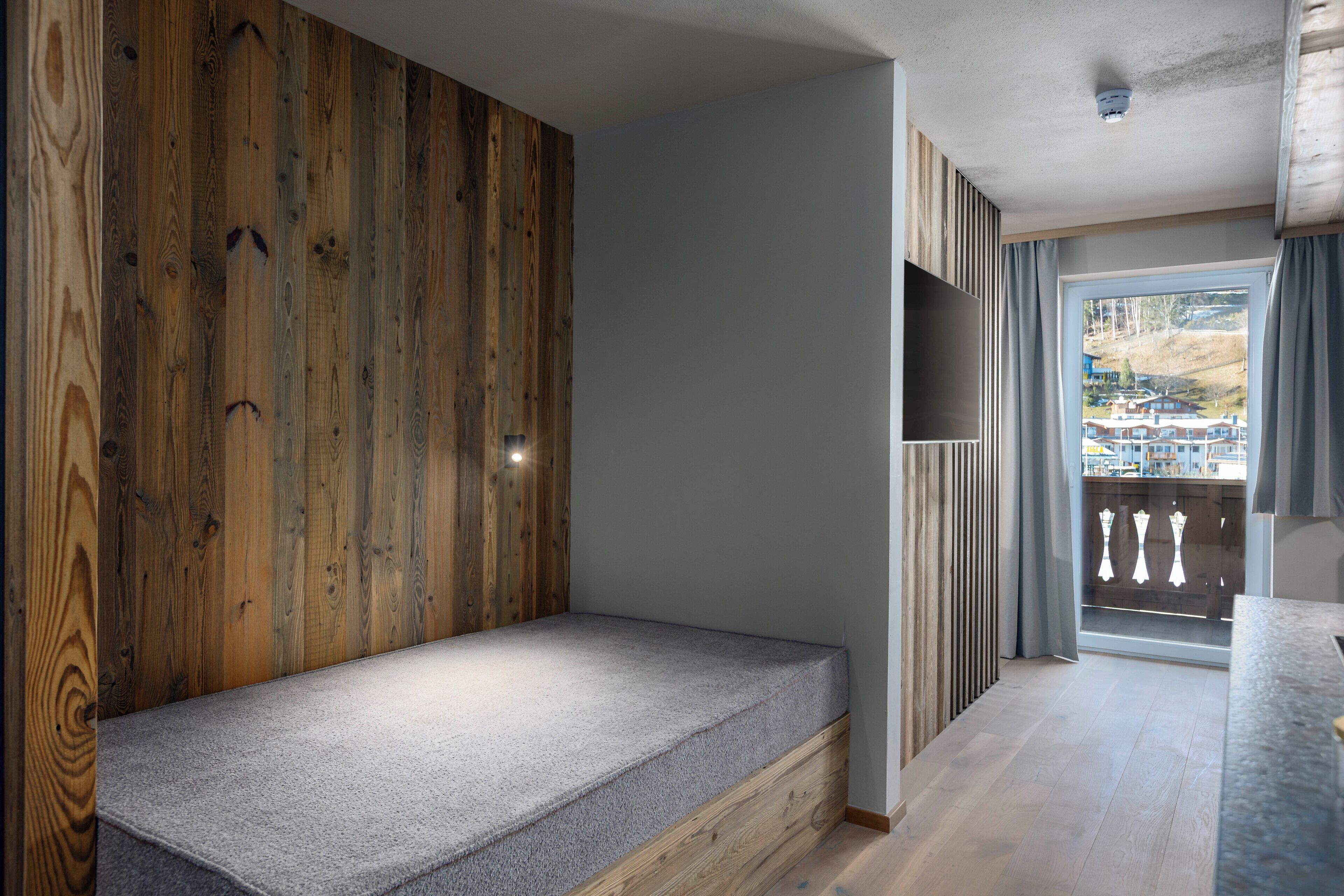 A room with a built-in bench, wooden panel wall, and a view of a balcony with curtains.