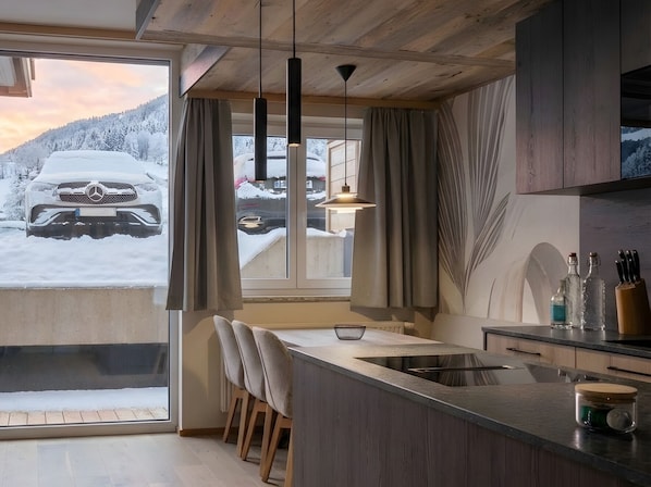 A modern kitchen with a large window, wooden ceiling, and bar stools. - Carpe Solem Kaprun Apartments by ALPS RESORTS (Kaprun)