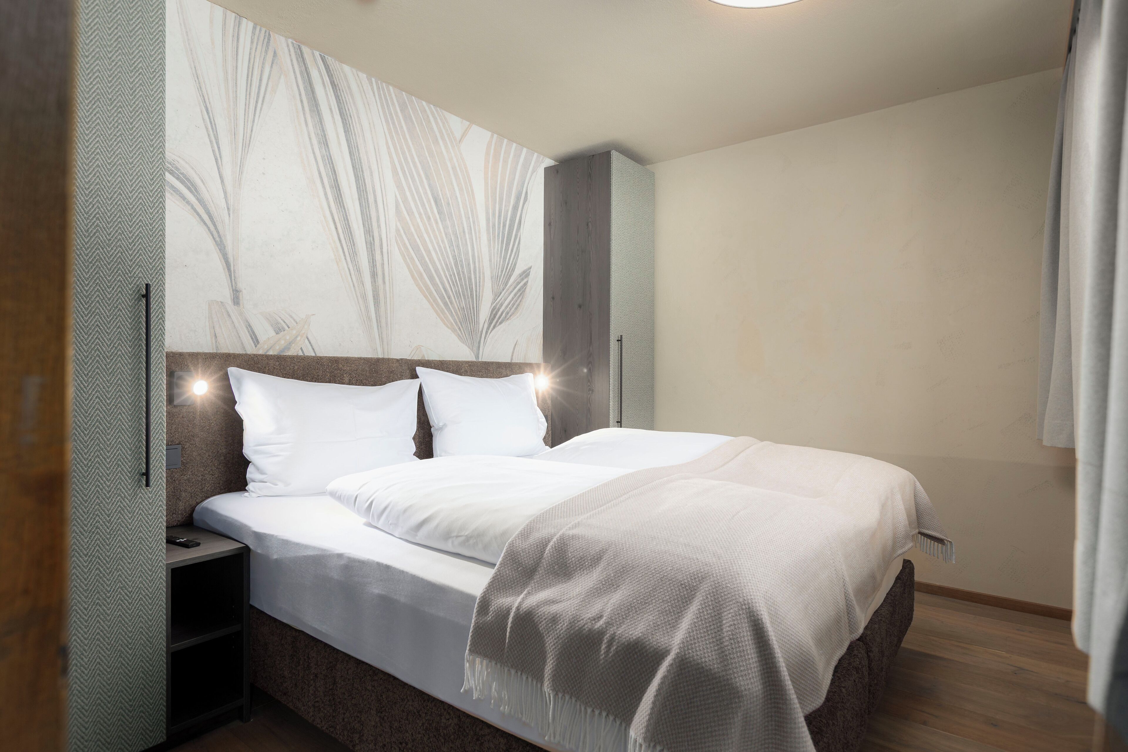 Une chambre à coucher moderne avec un grand lit, une table de chevet et une lampe fixée au mur.