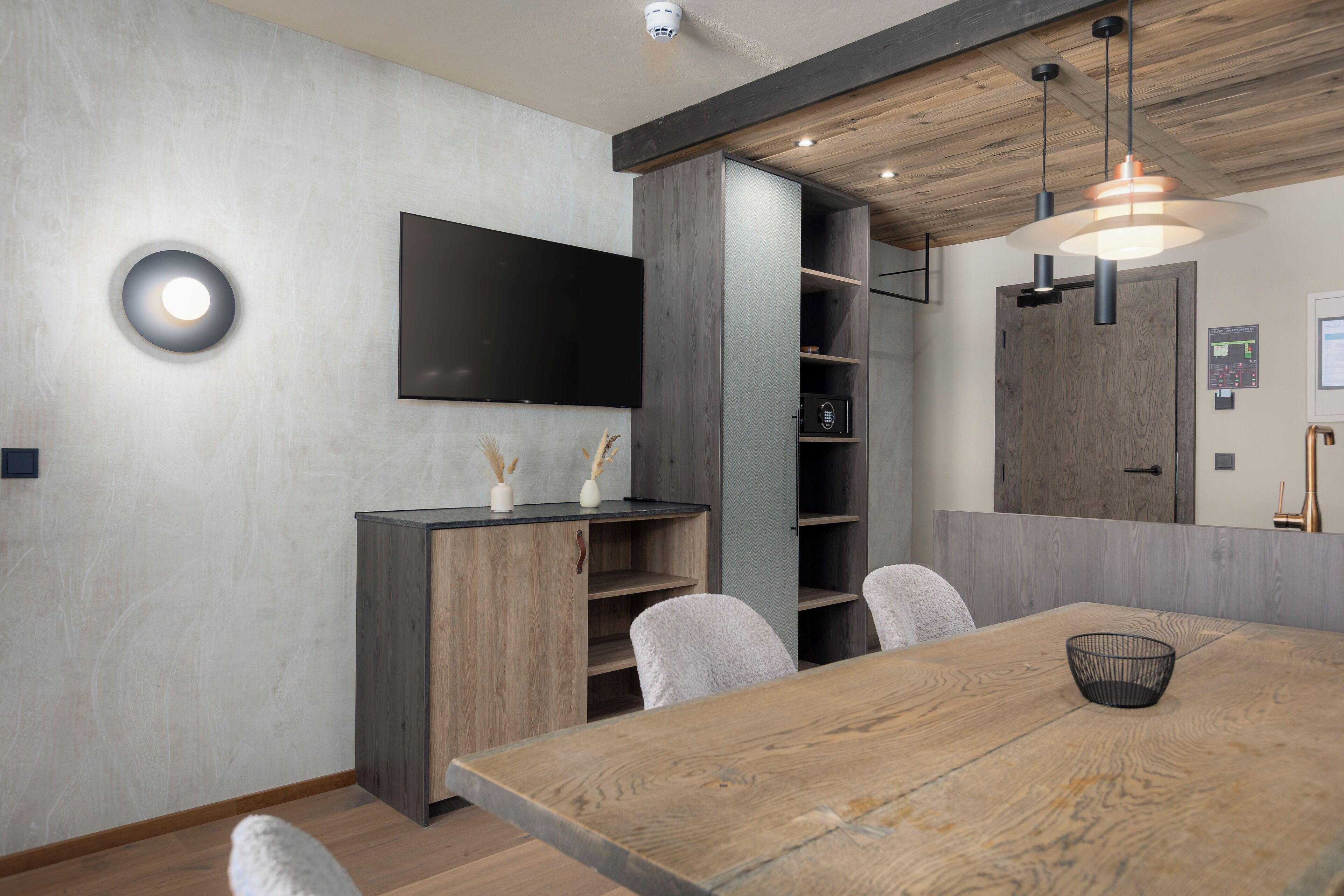 Een moderne eetruimte met een houten tafel, stoelen, een aan de muur bevestigde televisie en een inbouwkast.