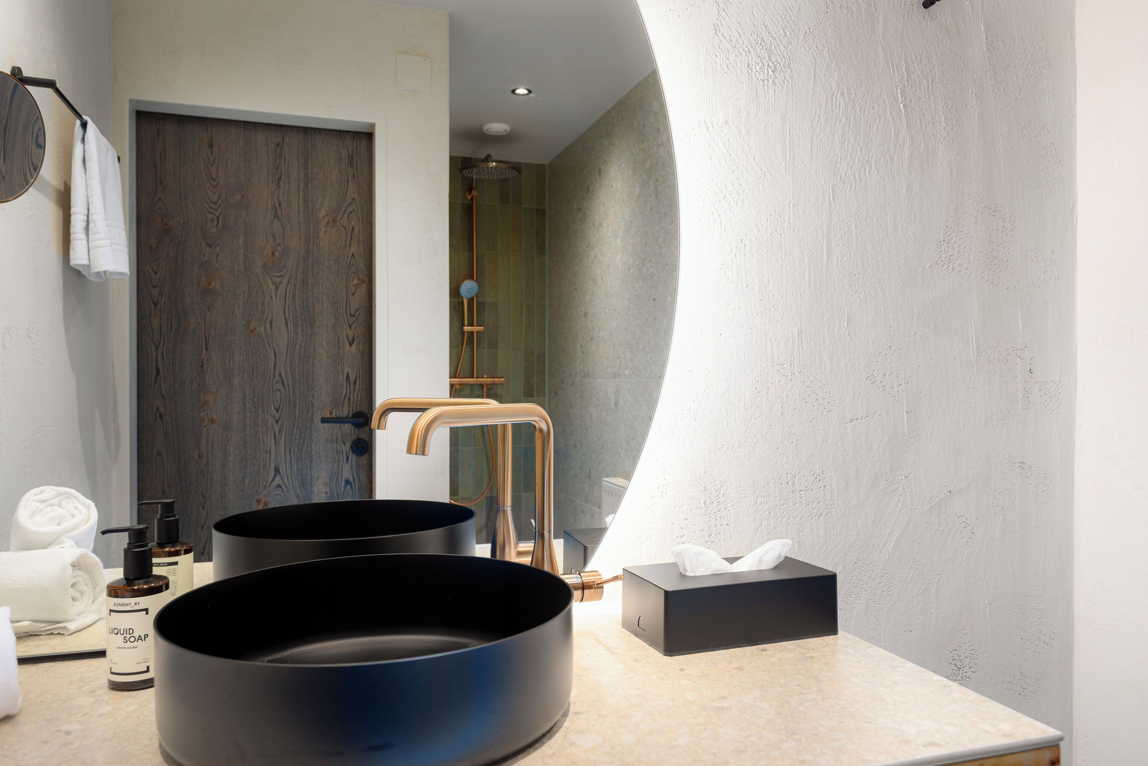 A modern bathroom with two round sinks, a wooden door, and a towel rack.