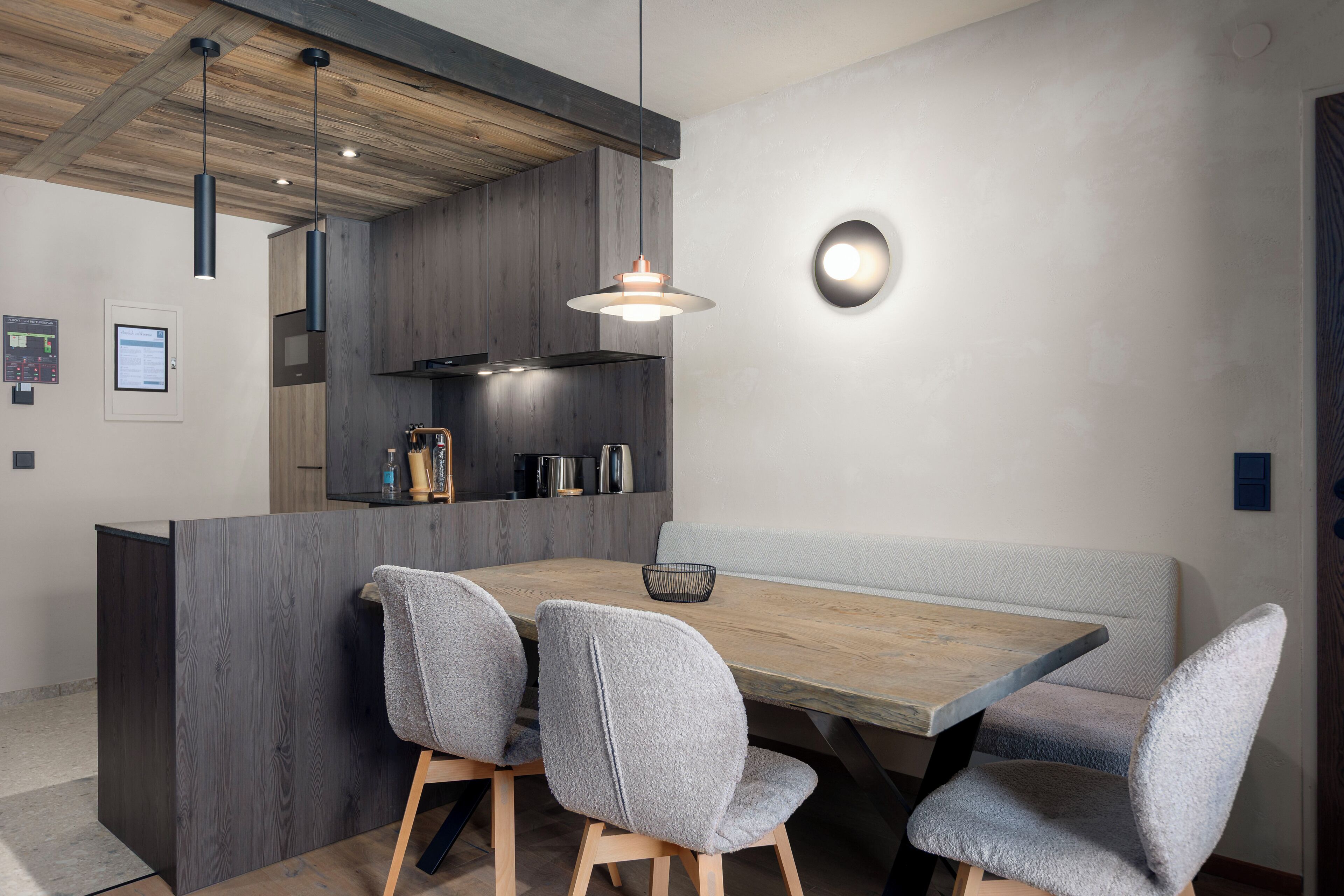 A modern dining area with a wooden table, grey upholstered chairs, and a built-in bench.