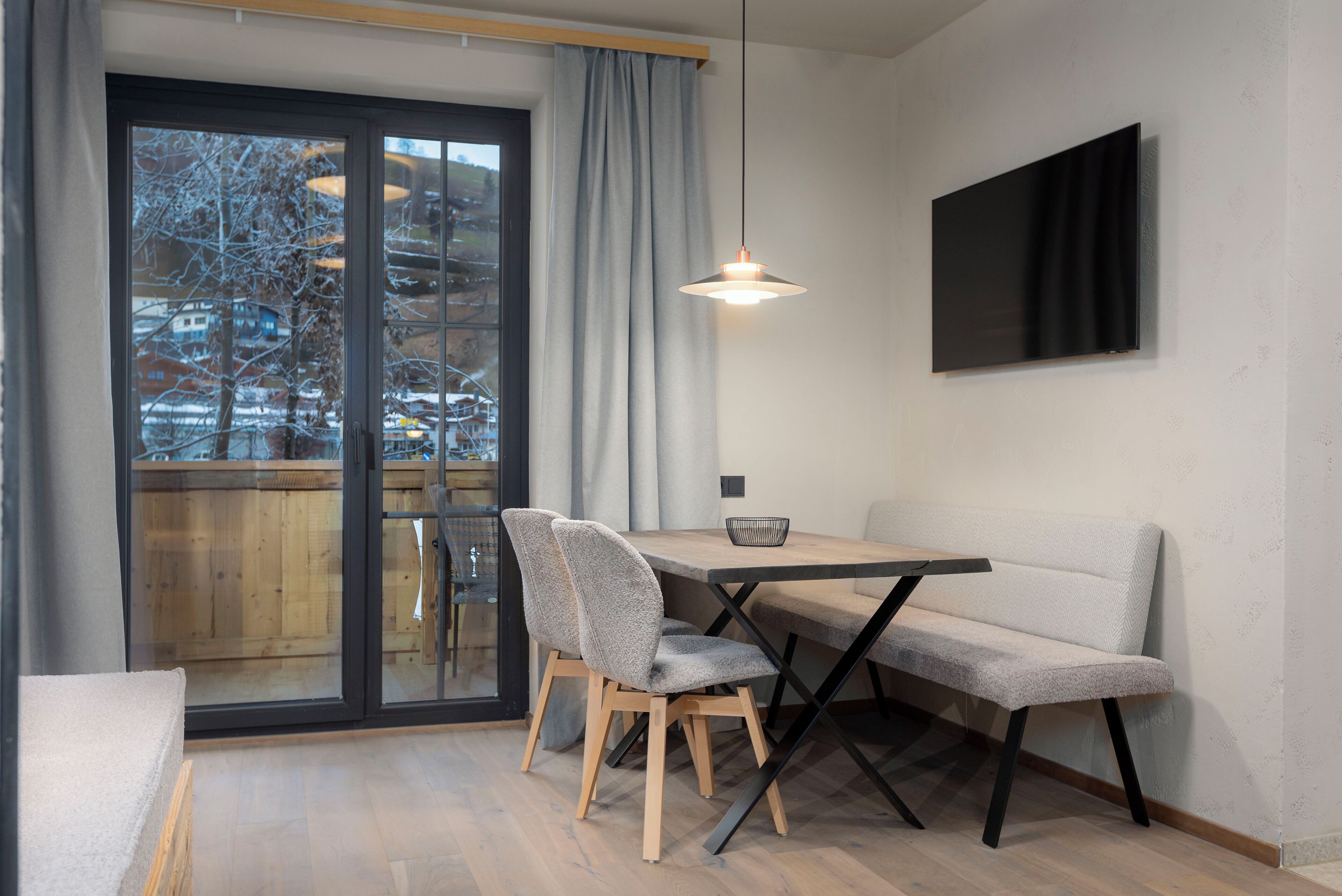 Ein moderner Essbereich mit Holztisch, zwei Stühlen und einer Bank, darüber eine Hängeleuchte.