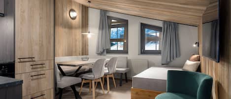 A modern, compact room with a wooden ceiling, a bed, a desk with chairs, and a television.