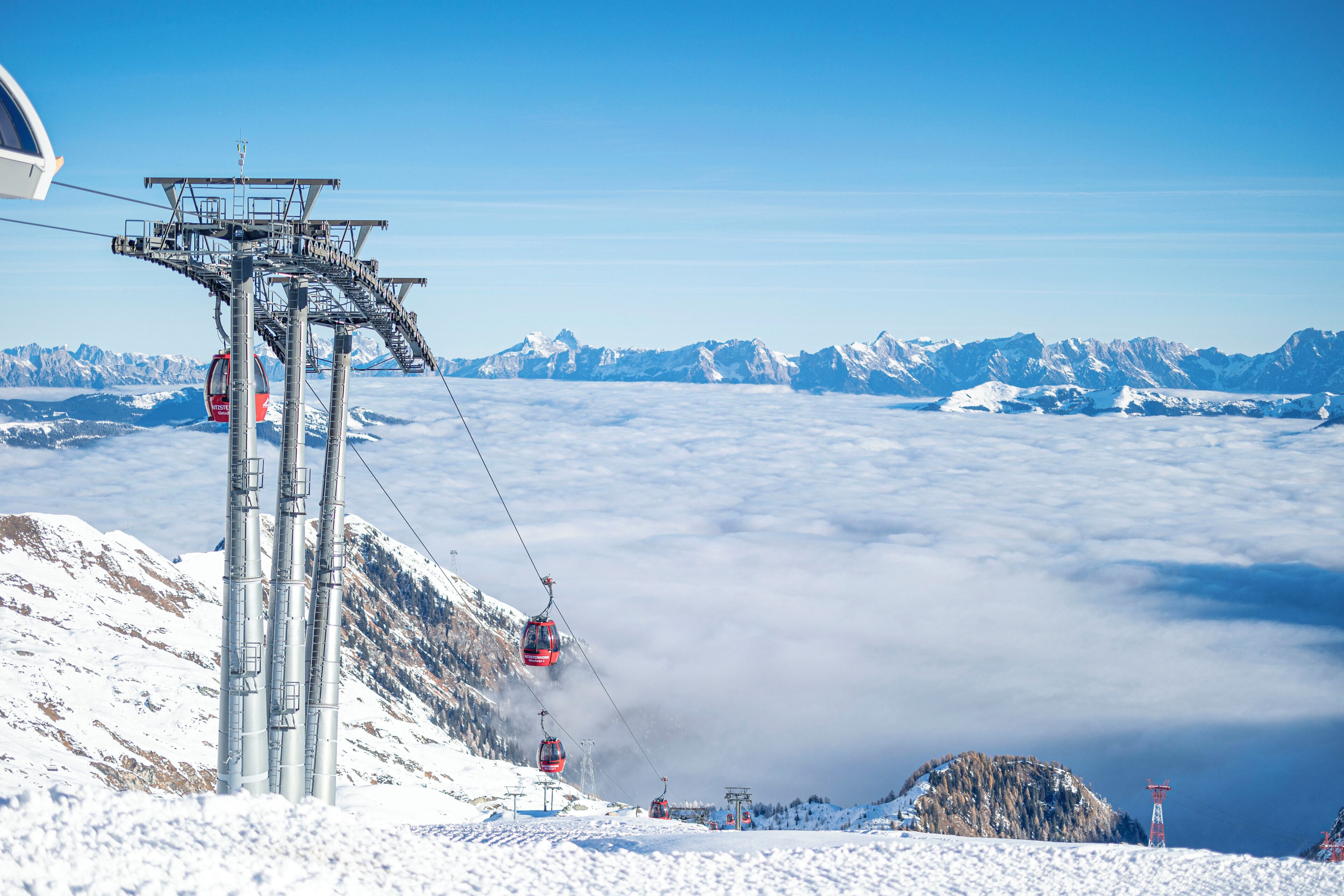 A cable car system with a clear view of snow-covered mountains and a cloud-covered valley below.