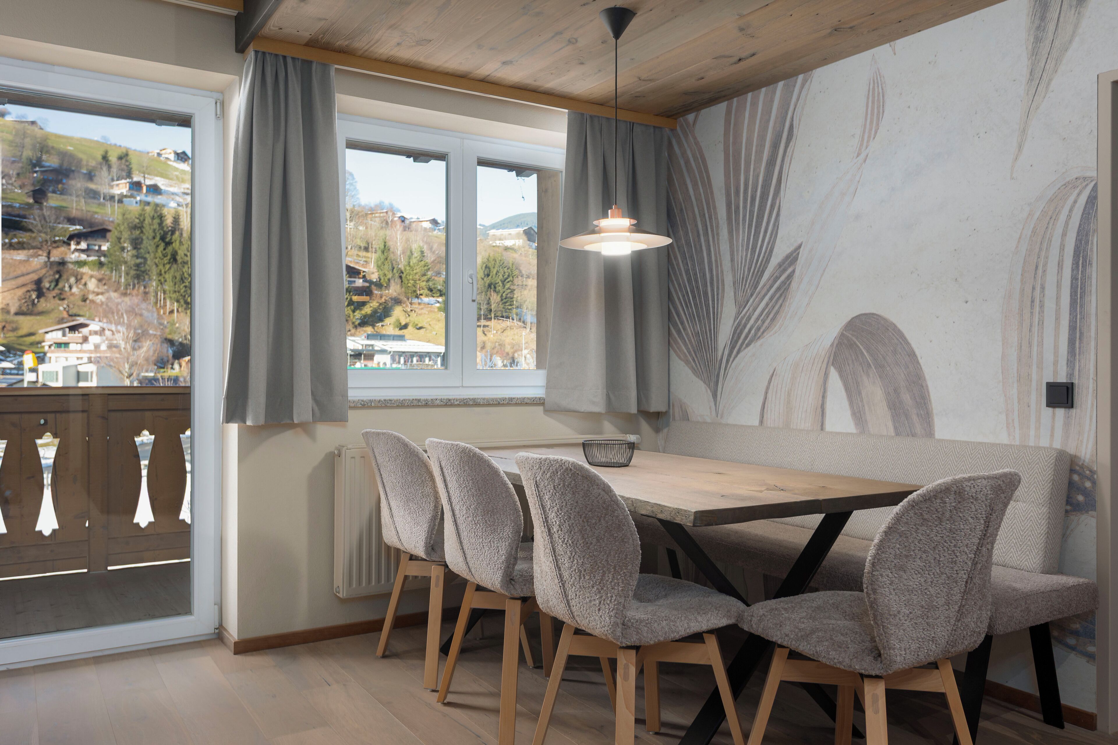 Un espace repas avec une table et des chaises en bois, une vue sur l’extérieur grâce à de grandes fenêtres et une fresque murale.