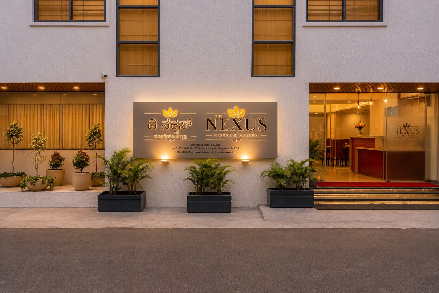 A hotel entrance with a signboard, potted plants, and a reception desk.