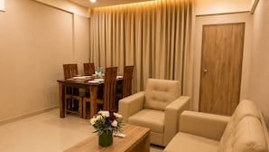 A living room with a sofa, armchair, wooden coffee table, and a dining area with chairs and a table. - The Nexus (Bengaluru)