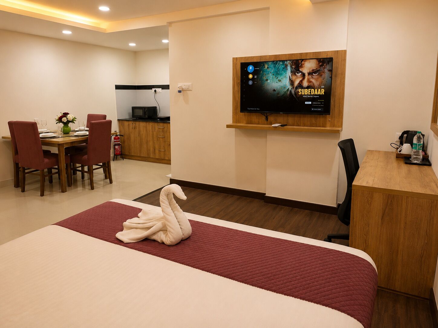 Ein Hotelzimmer mit Bett, Wandfernseher, Schreibtisch und Essecke mit Stühlen und Tisch.