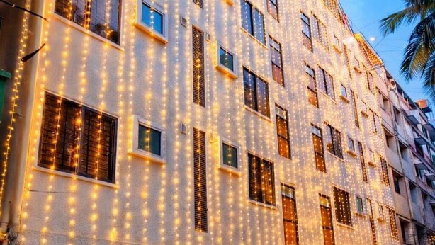 A multi-story hotel with string lights, potted plants, and a visible entrance. - The Nexus (Bengaluru)