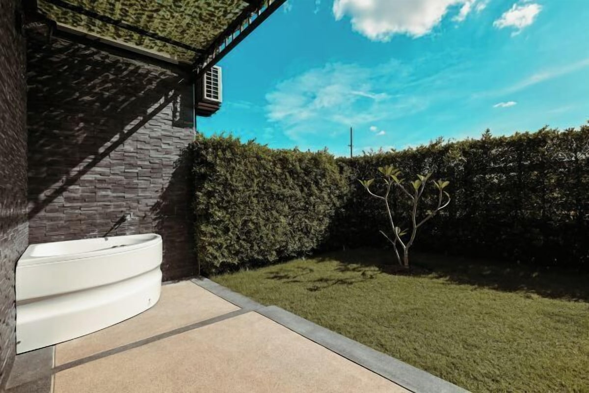 A modern outdoor bathroom with a built-in bathtub, surrounded by a well-maintained hedge and a clear blue sky.