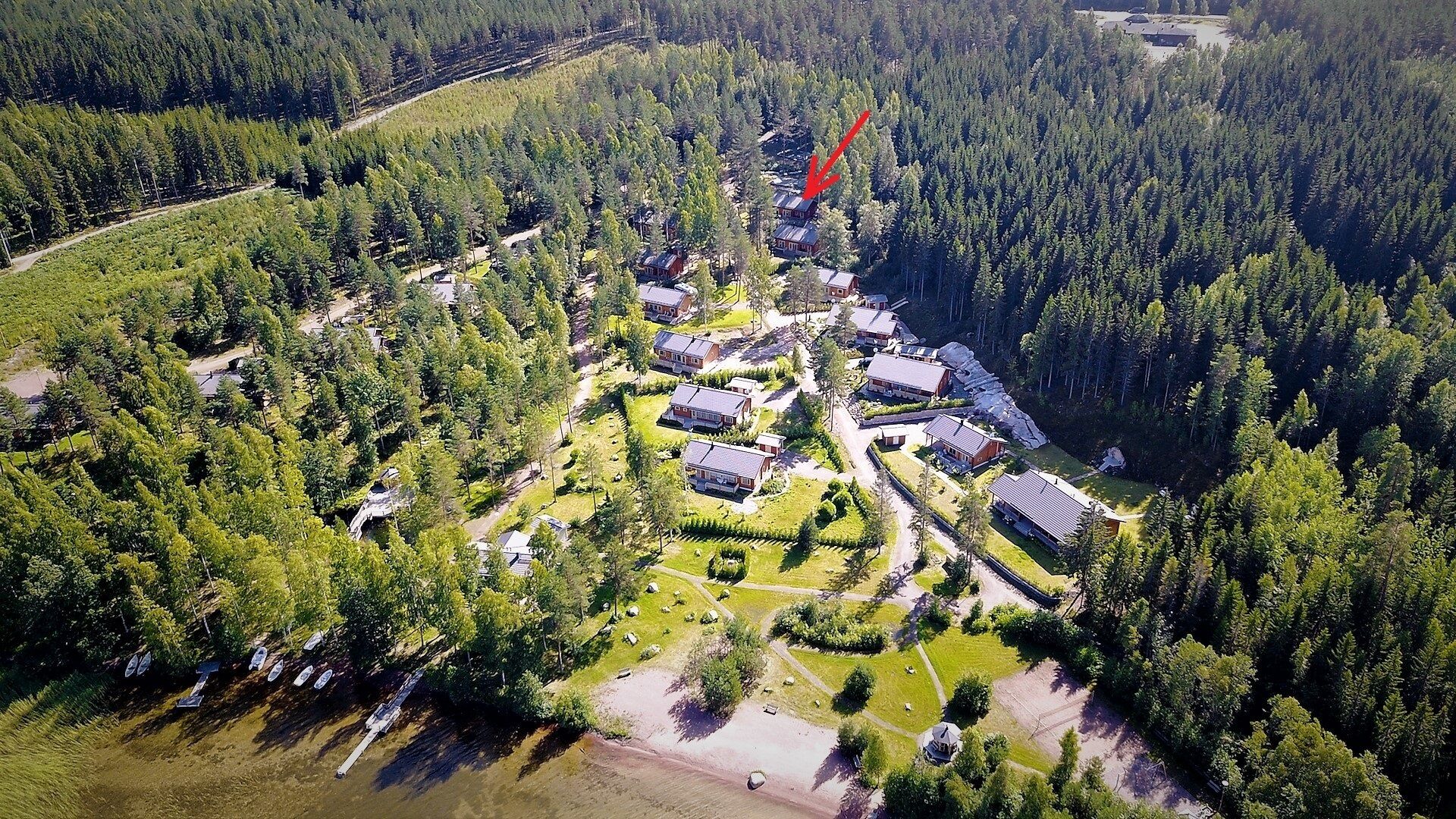 Une vue aérienne d’une zone boisée comprenant plusieurs bâtiments, des routes et une grande étendue d’eau.