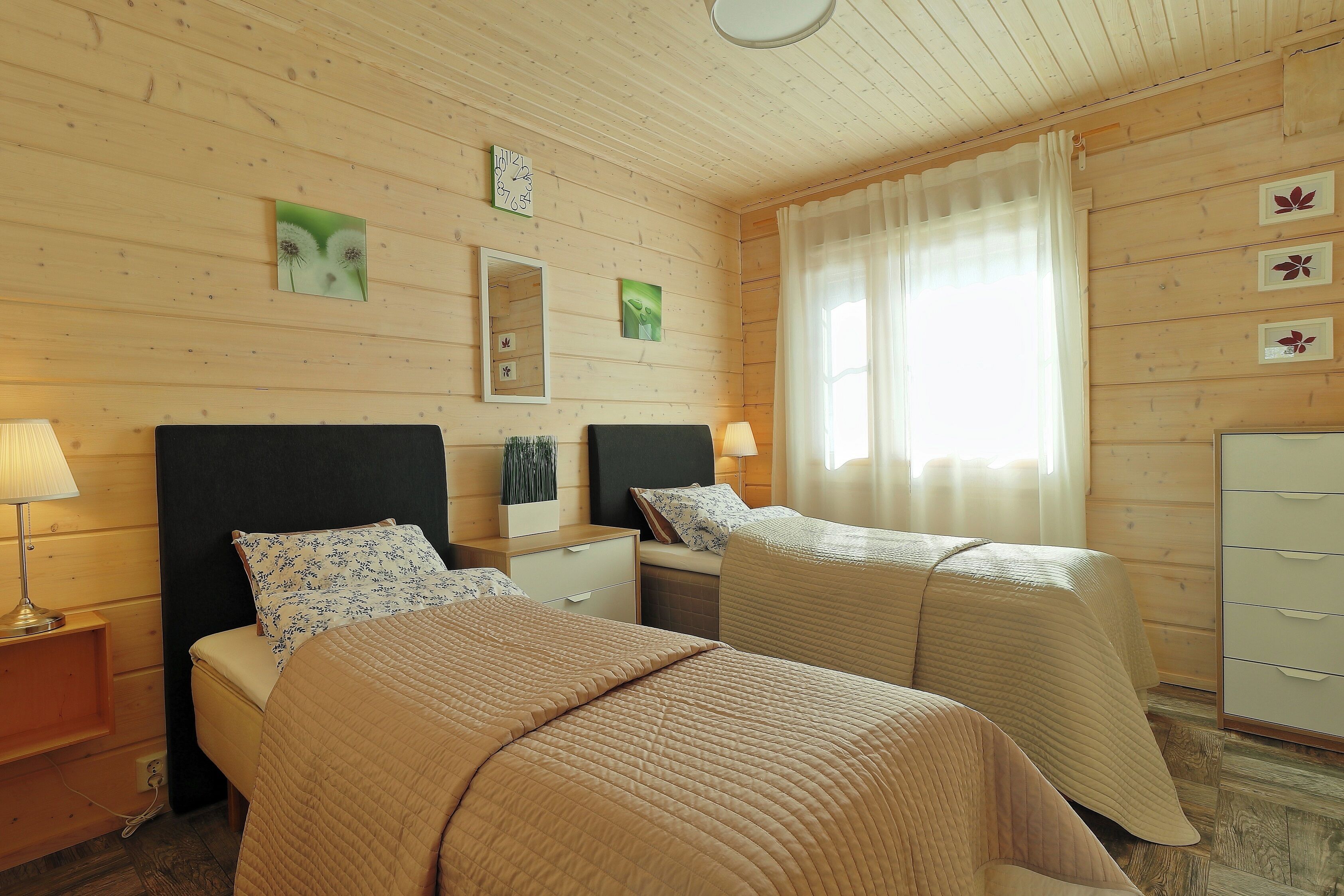 Een kamer met twee bedden, houten wanden, een spiegel, een dressoir en een raam met gordijnen.