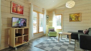 Una sala de estar acogedora con piso de madera, un tapete de cuadros, un sofá verde, un mueble de televisión de madera y un gran ventanal con cortinas.
