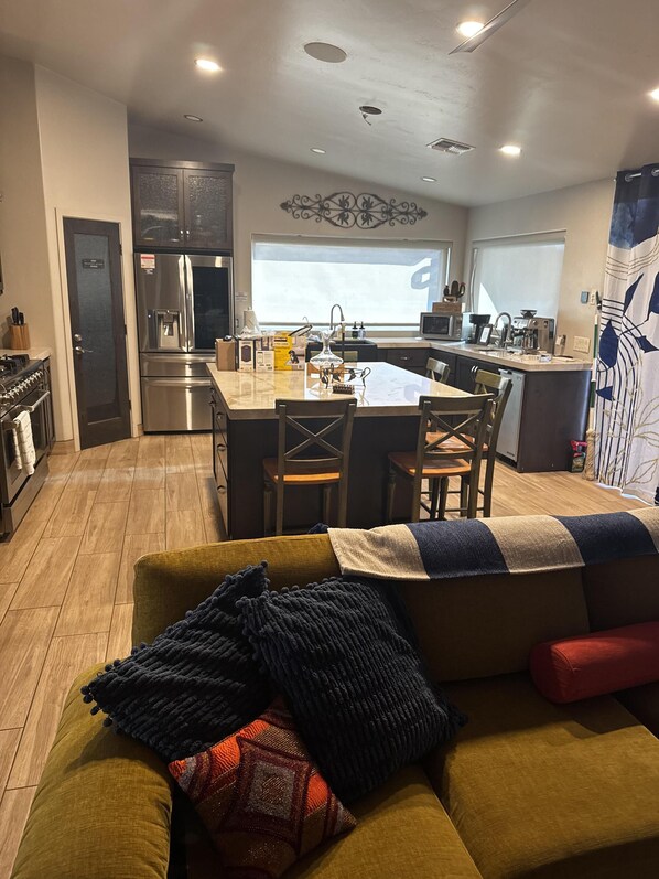 A modern kitchen with a central island, stainless steel appliances, and a dining area with a yellow sofa. - Grand Sand Riverfront, private beach & boat dock (Parker)