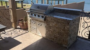 An outdoor grill area with a stone countertop, a table, and a chair. - Grand Sand Riverfront, private beach & boat dock (Parker)