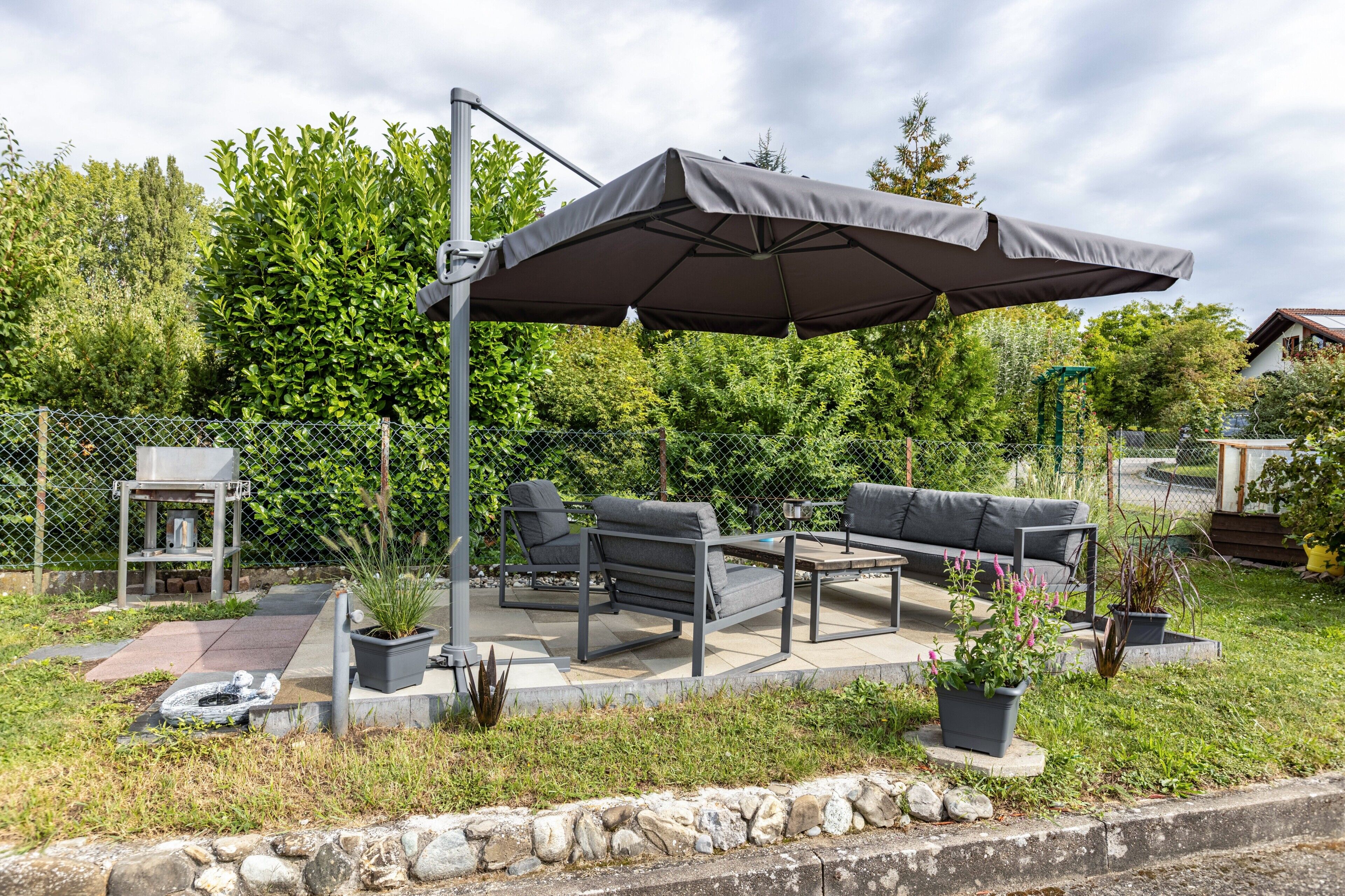 An outdoor patio with a covered seating area, a grill, and potted plants.