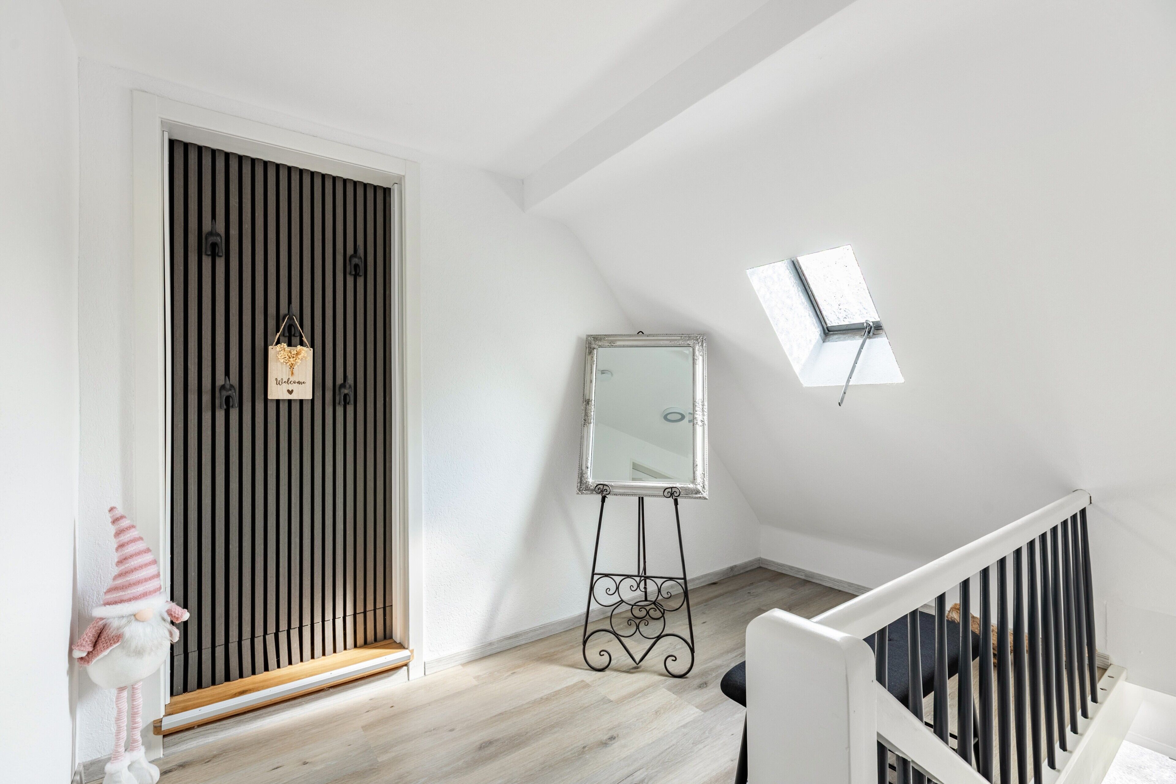 A room with a sloped ceiling, a white door with vertical blinds, a standing mirror, and a small skylight.